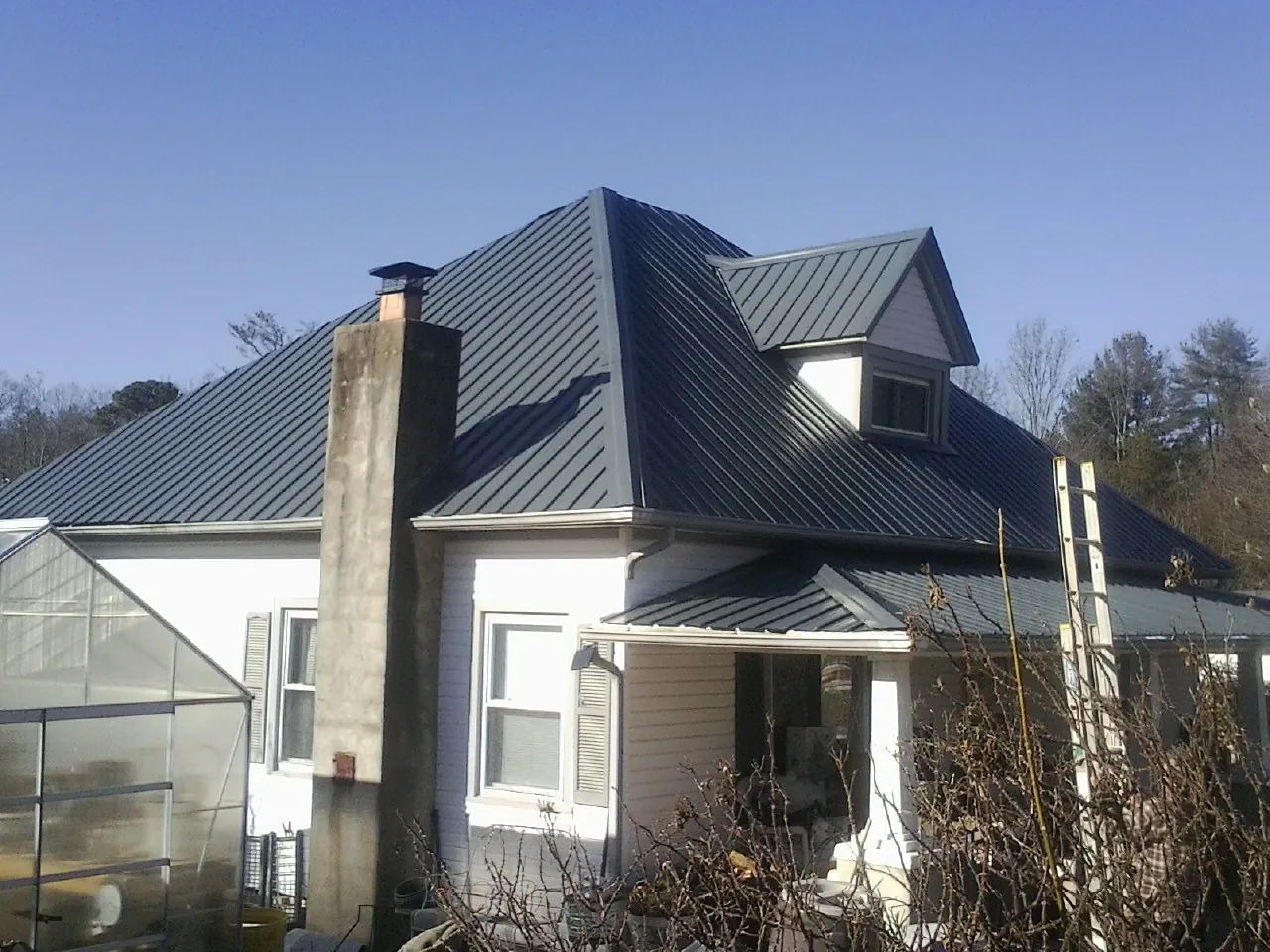 Dark blue standing seam metal roof on a white farmhouse with dormer — Slate & Tile Roof Repair by Roofing Brothers in West Grove