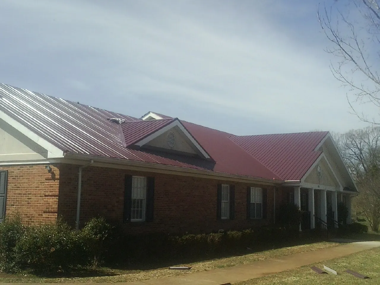 Red metal roof with gabled entries on a long brick building, from a Hail Damage Roof Repair job in West Grove