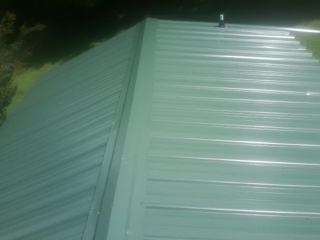 New green metal panels meeting at the ridge of a roof — Flat Roof Repair work by our crew in West Grove