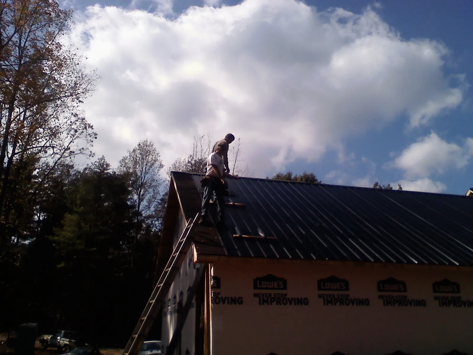Roofer fastening dark metal panels high against a cloudy sky, from a Roof Inspection job in West Grove