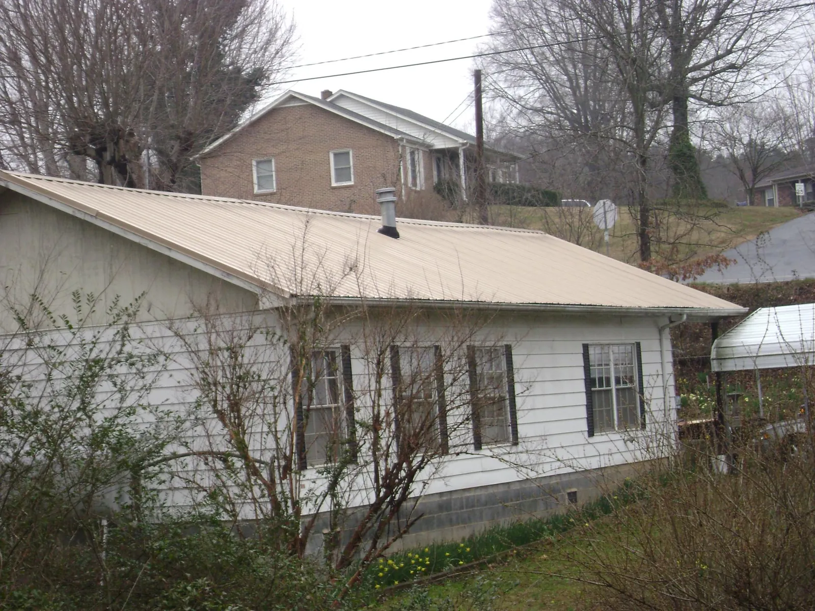 Tan metal roof on a white sided house set into a hillside — Commercial Roofing by Roofing Brothers in West Grove