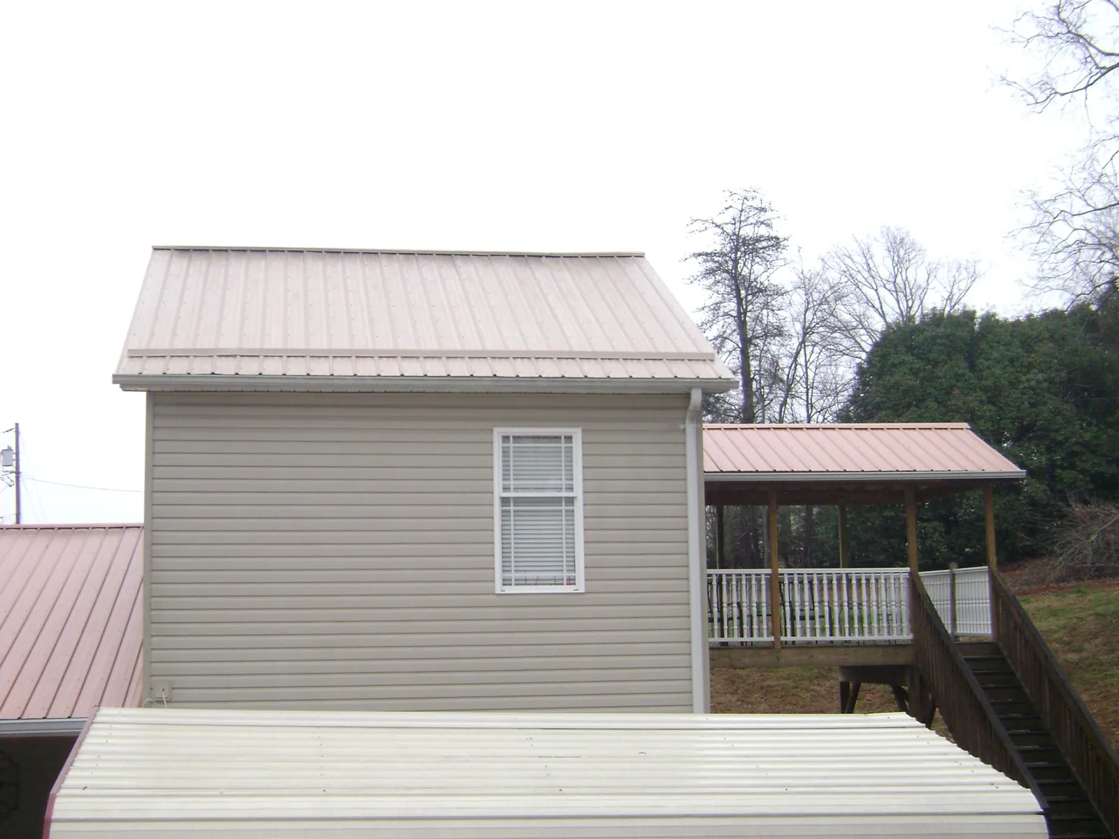 Tan metal roofs on a two story addition and attached porch, from a Roof Replacement job in West Grove